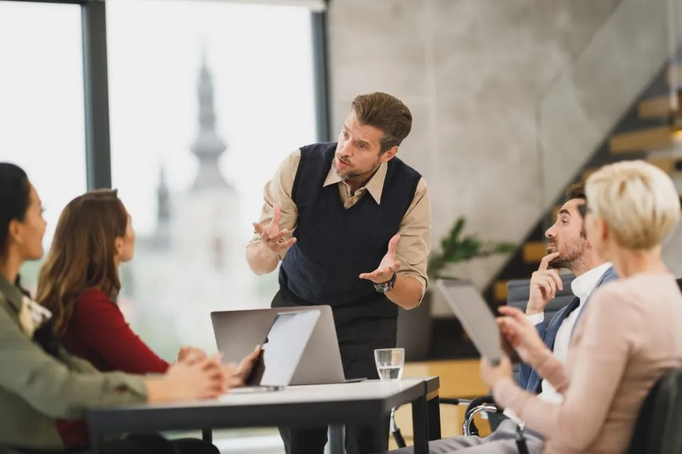 Equipo de trabajo conversando alrededor de una mesa con laptops