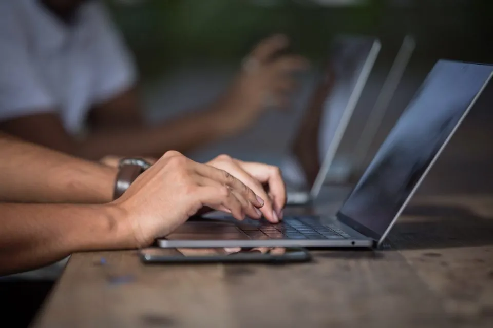 Manos escribiendo en una laptop sobre una mesa de madera
